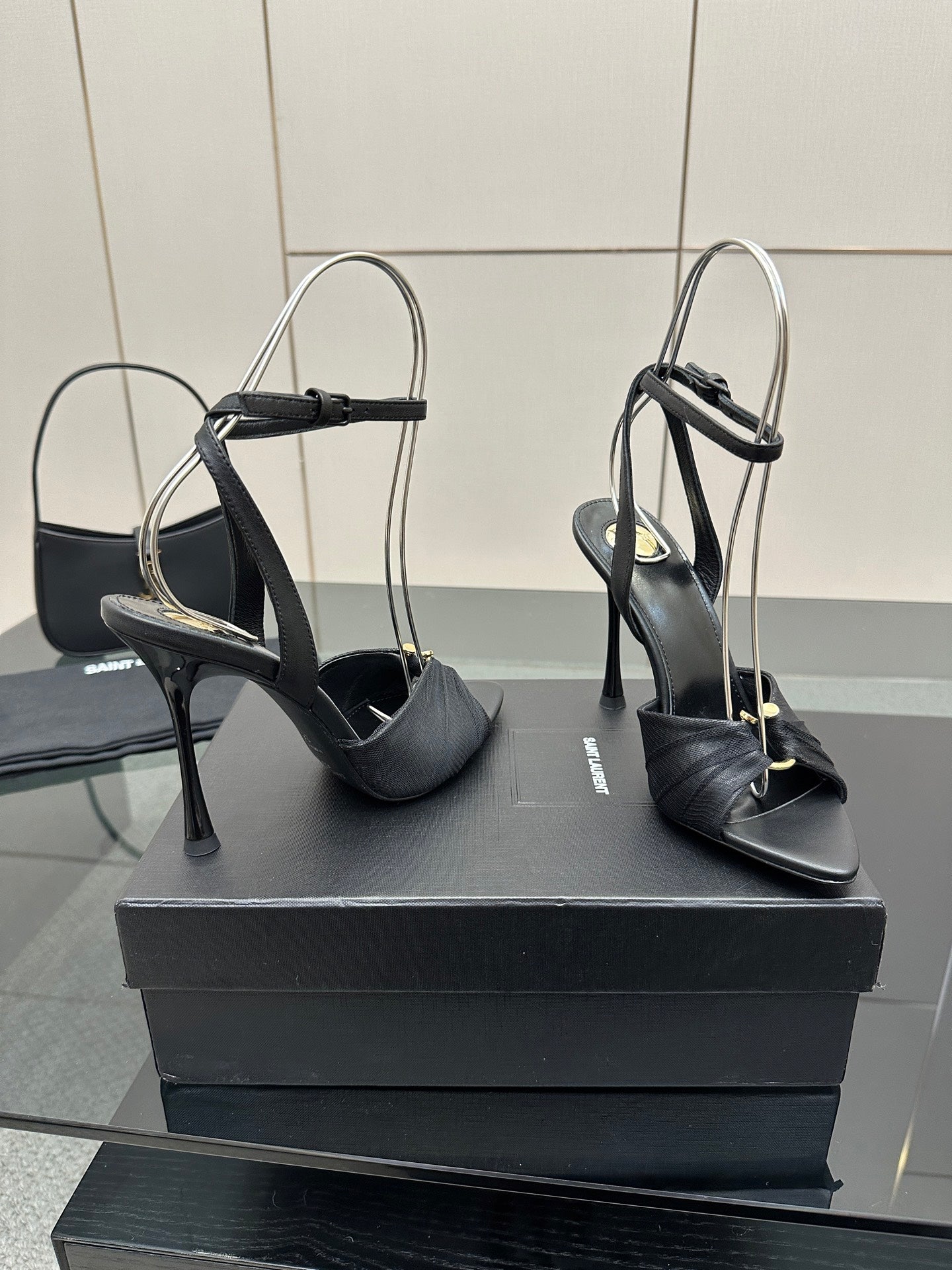 Black open-toe stiletto heeled sandals with slim heel and ankle strap, on box