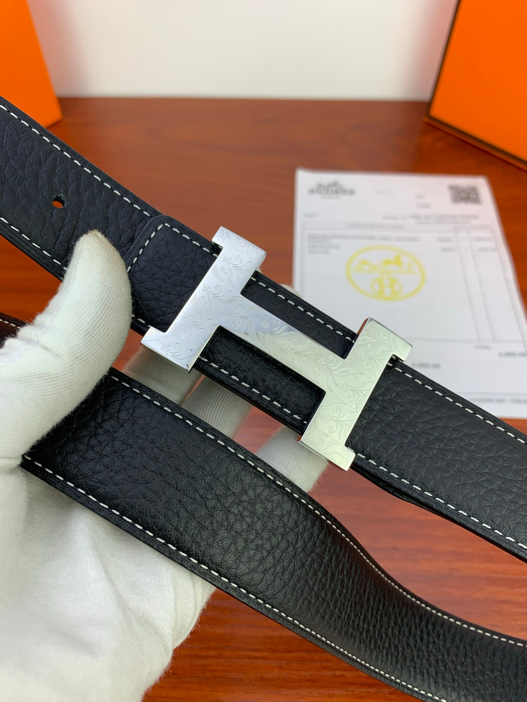 Hermes belt close-up with black leather, light stitching, and metal buckle elements