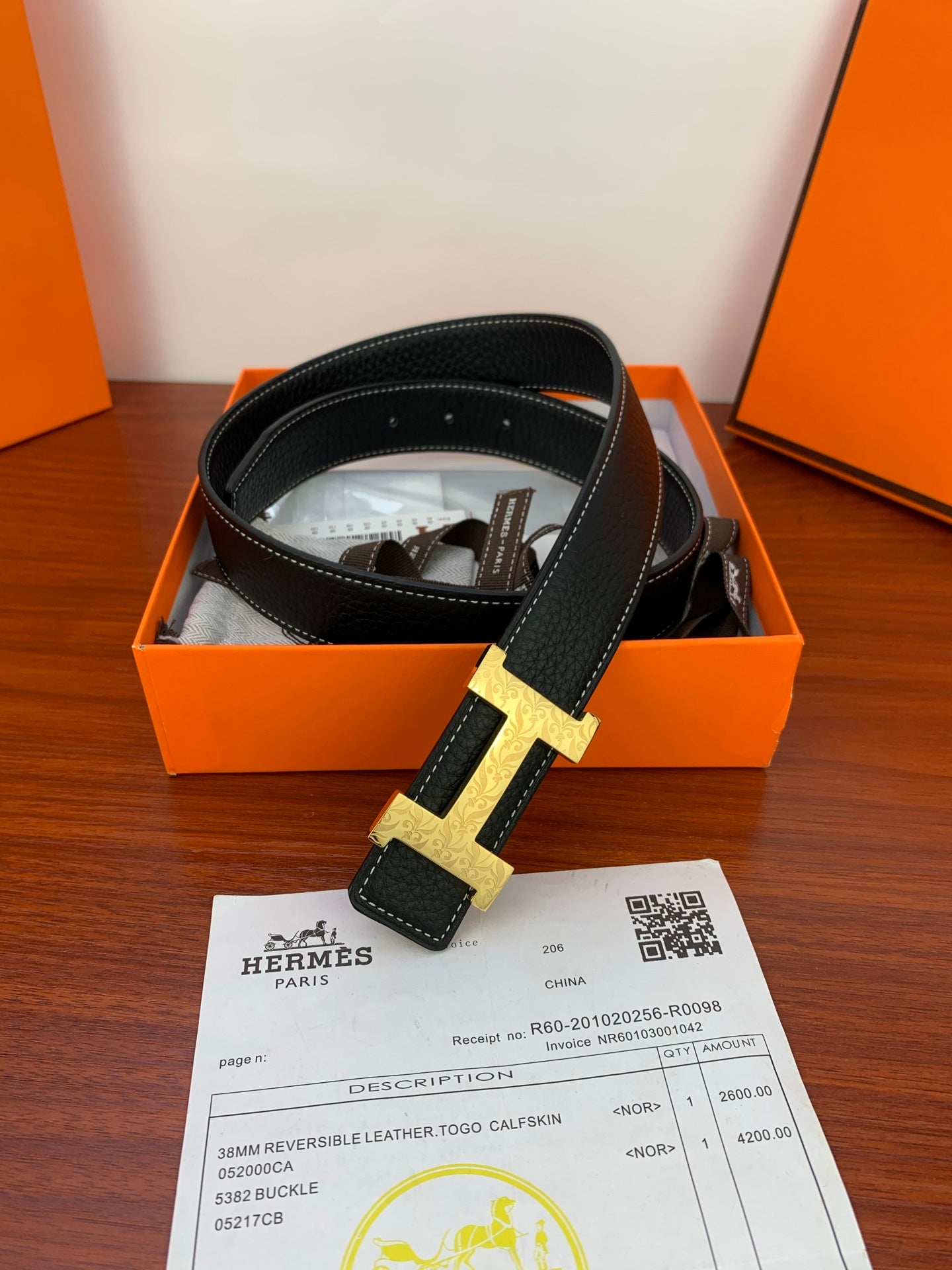 Hermes belt with black strap and gold H buckle, laid over box and receipt
