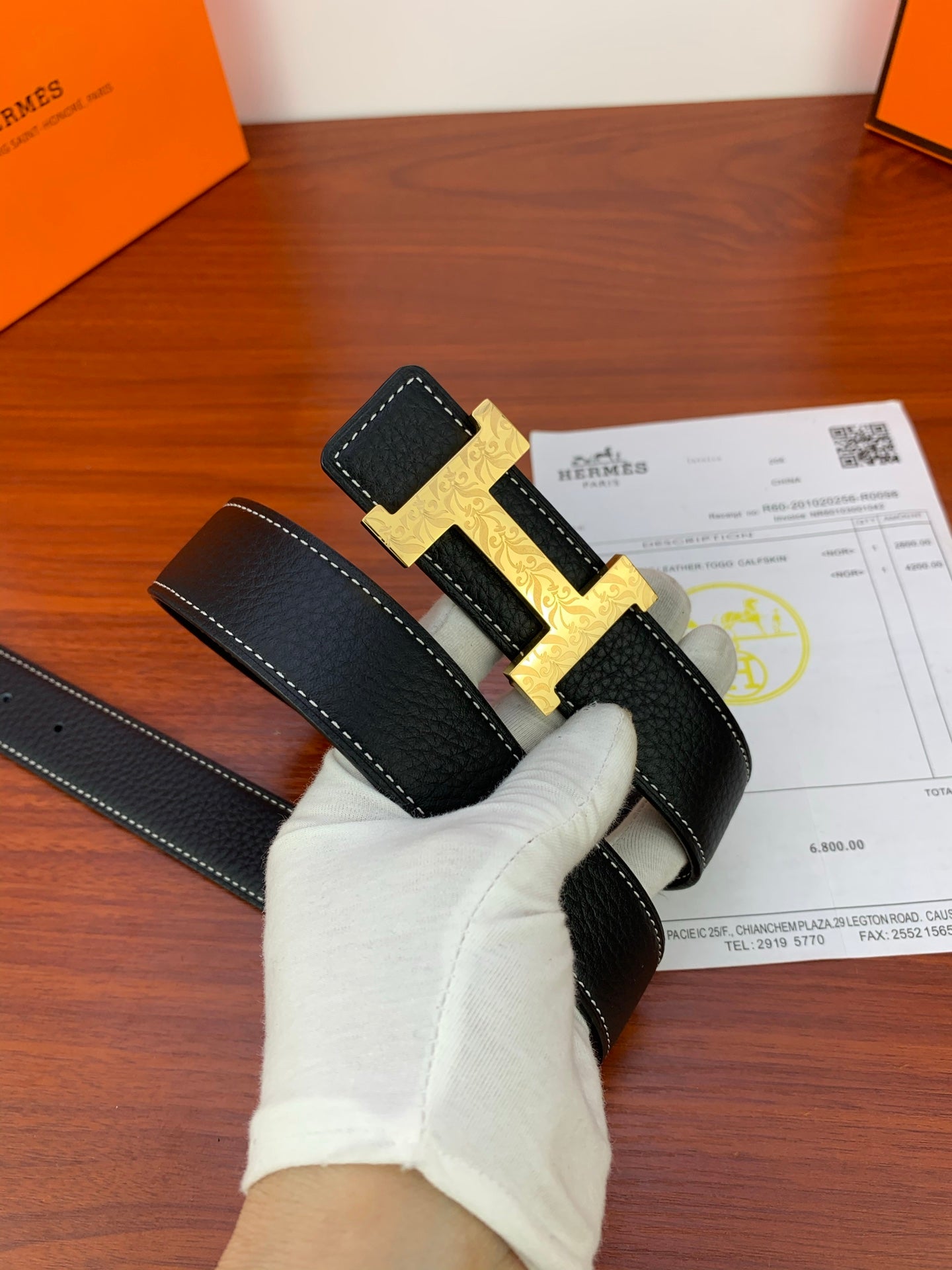 Hermes belt on hand view with gold H buckle and black leather strap