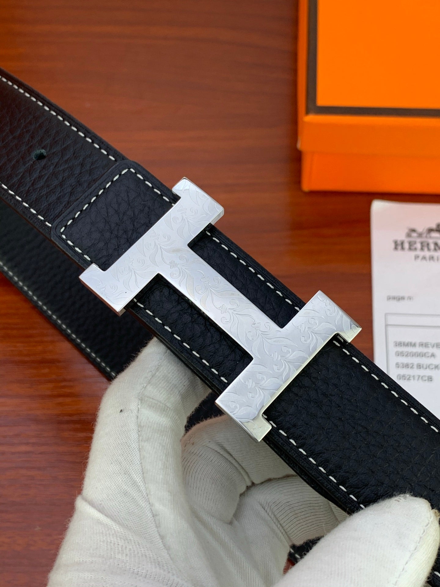 Hermes belt close-up with black textured leather and white-stitched pattern on buckle