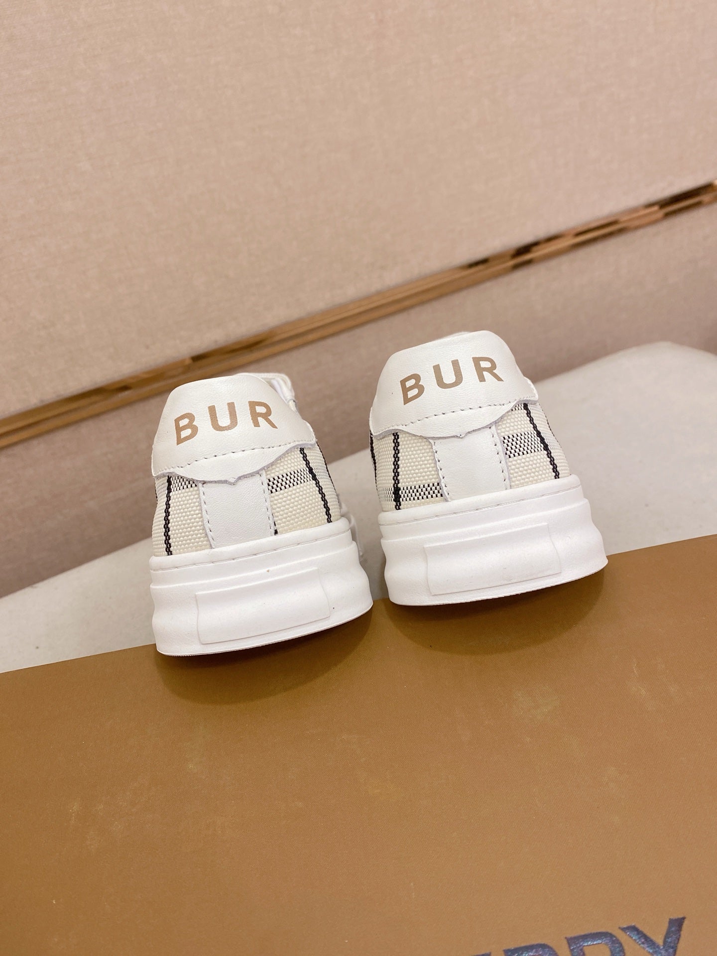 Back view of white Burberry sneakers with “BUR” logo on heels and white sole