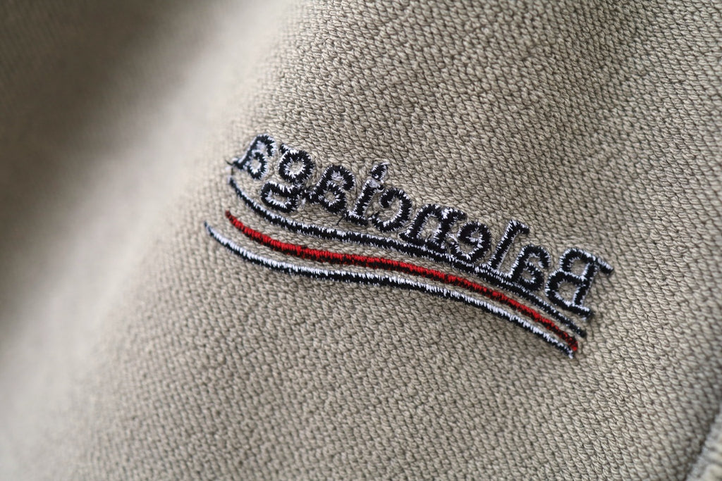 Beige fabric logo patch with embroidered text and multicolor stripe