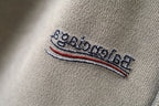 Beige fabric logo patch with embroidered text and multicolor stripe