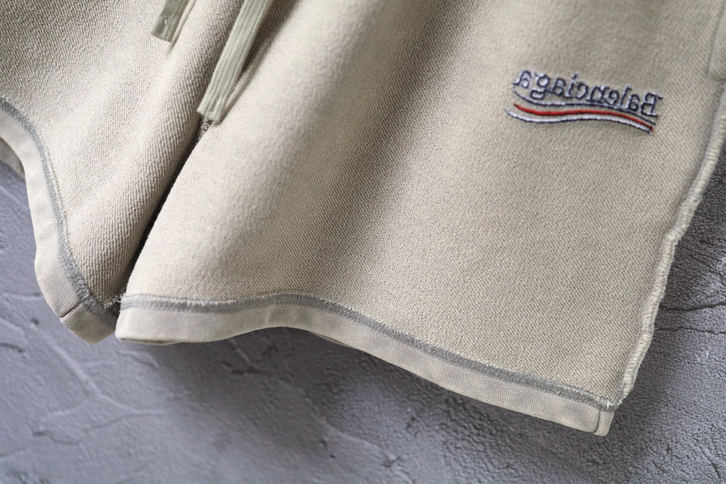 Beige shorts hem with contrast stitching and small logo patch