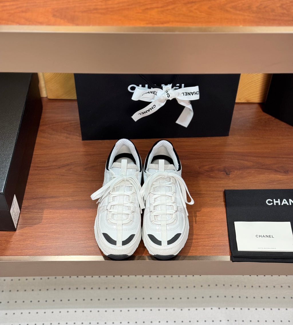Pair of white Chanel unisex sneakers with black trim and lace-up design