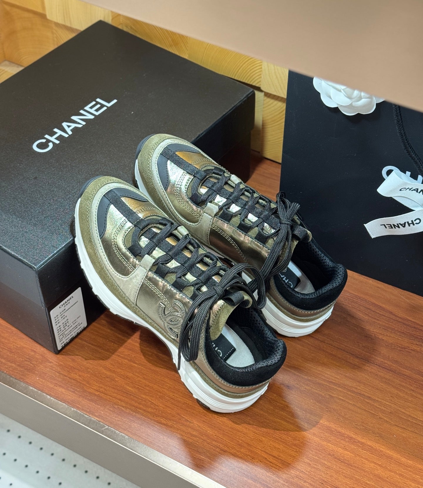 Pair of Chanel sneakers on display: olive-gold uppers with black laces and white soles