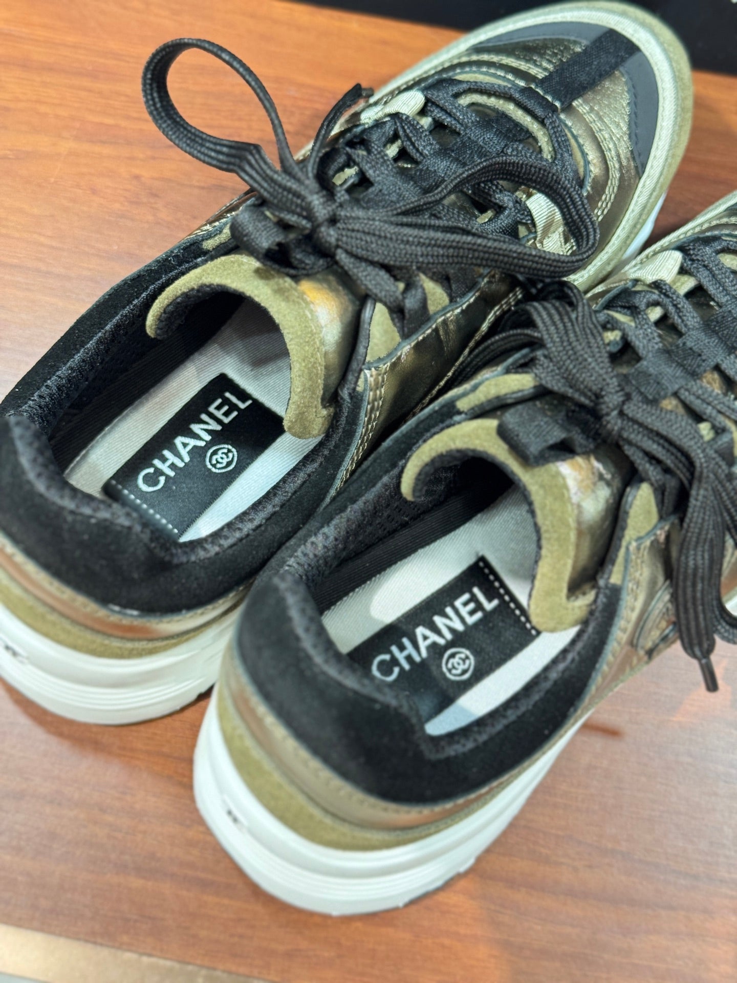 Chanel sneakers close-up: olive-gold fabric with black laces and branded tongue labels