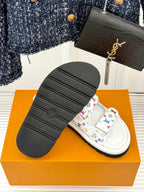 Black outsole of a white slide sandal with multicolor monogram strap
