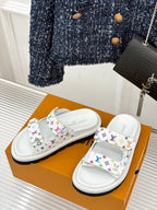 Pair of white slide sandals with multicolor monogram straps, shown on a box