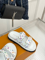 White slide sandals with multicolor monogram straps, side view on a box