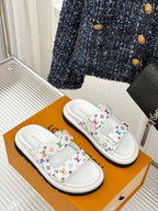 White slide sandals with multicolor monogram straps, angled view on a box