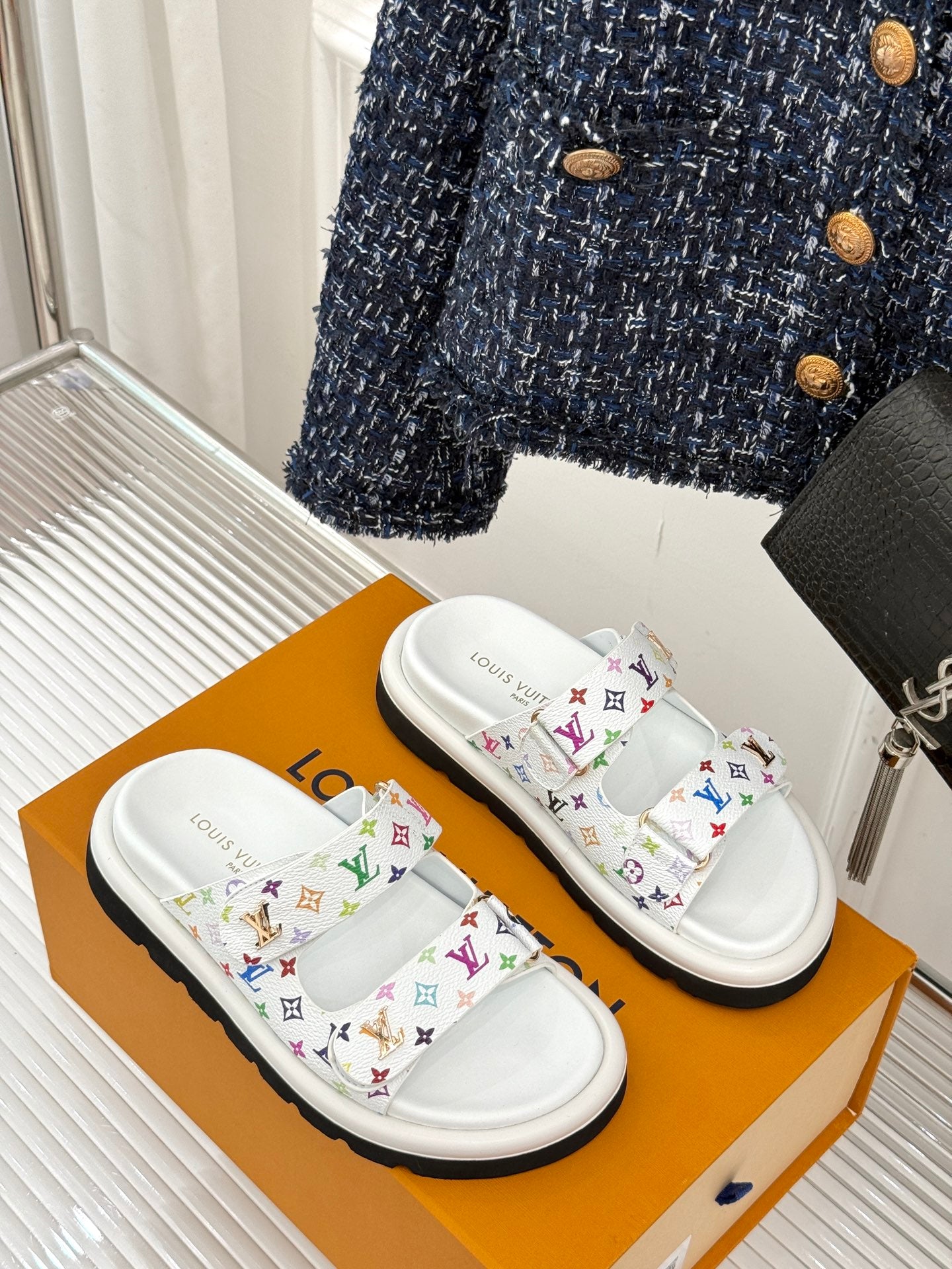 White slide sandals with multicolor monogram straps, angled view on a box