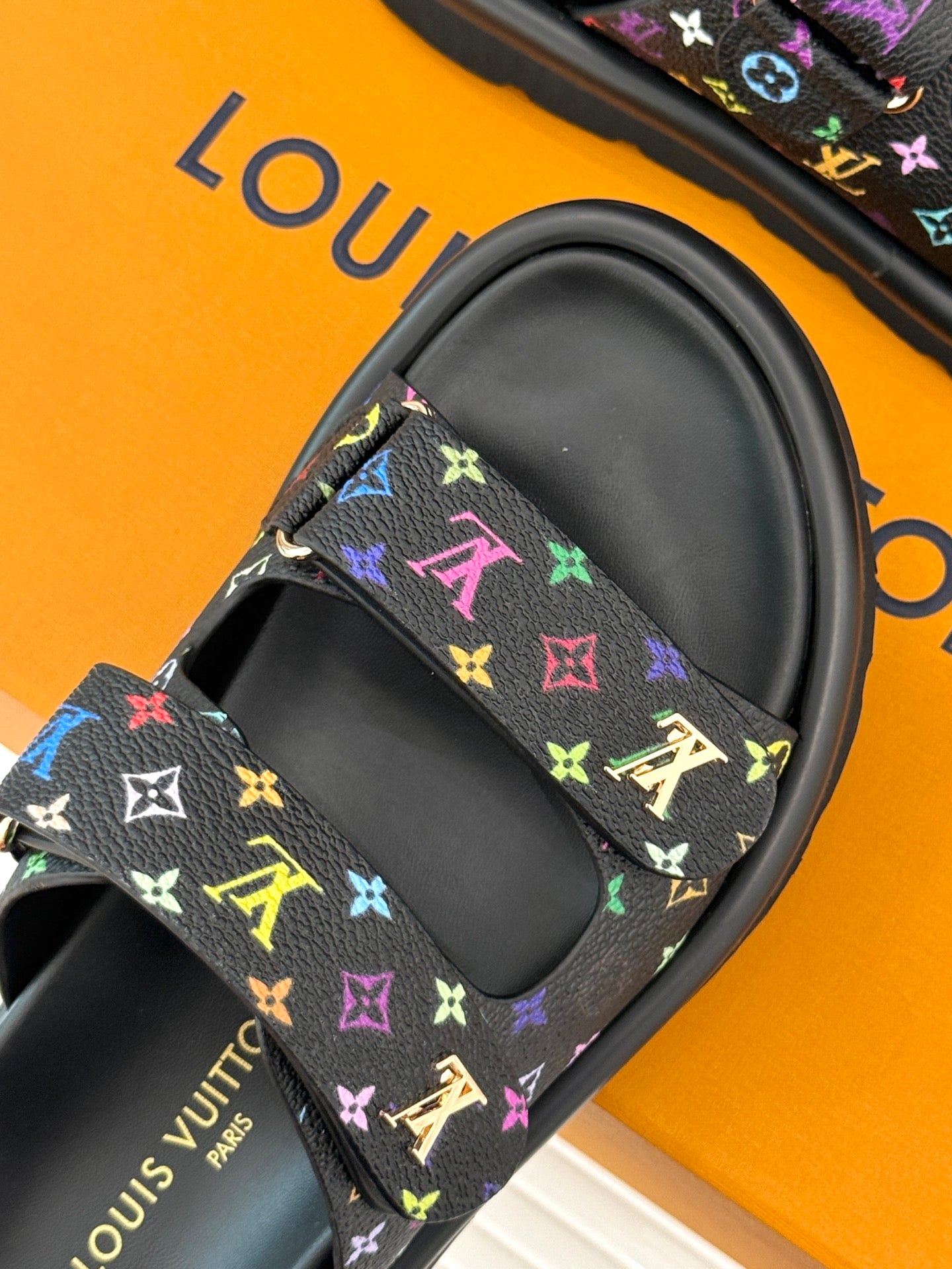 Close-up of Louis Vuitton slide sandal strap with multicolor monogram pattern on black
