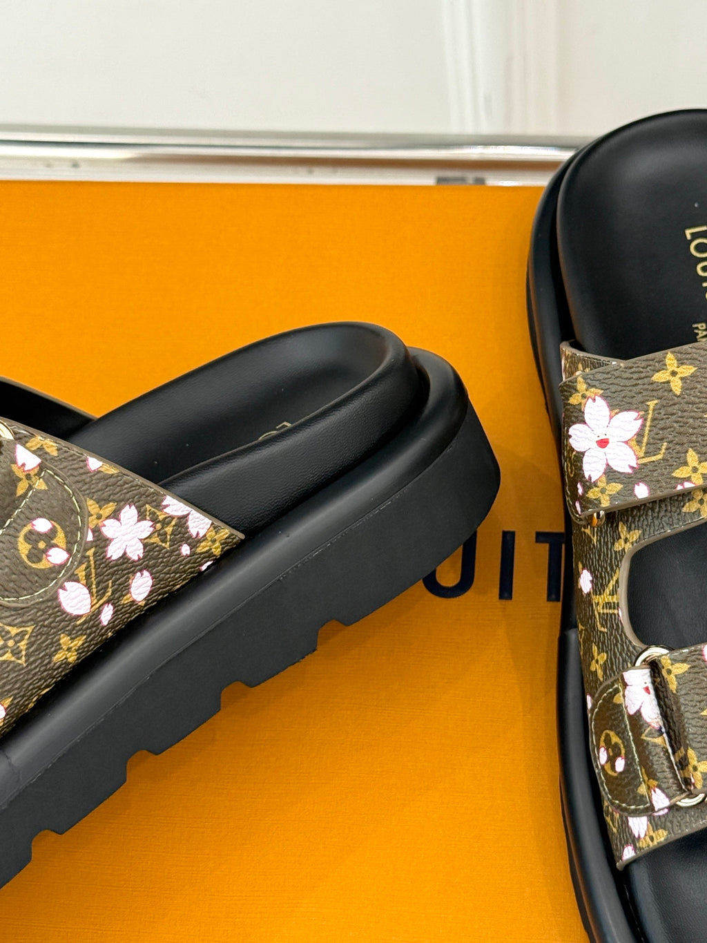Ladies slide sandals with black slide bands and brown floral monogram accents