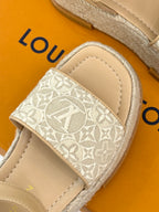 Close-up of beige espadrille sandal showing white monogram strap and stitched edge