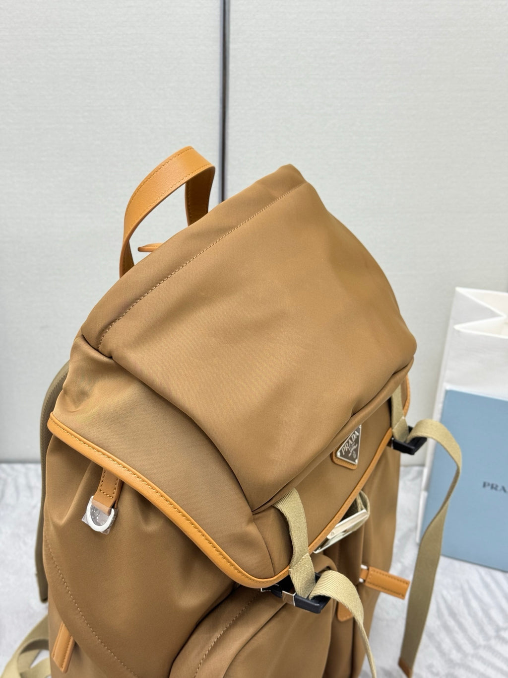 Prada tan backpack with side flap and buckle strap, showing top and front seams