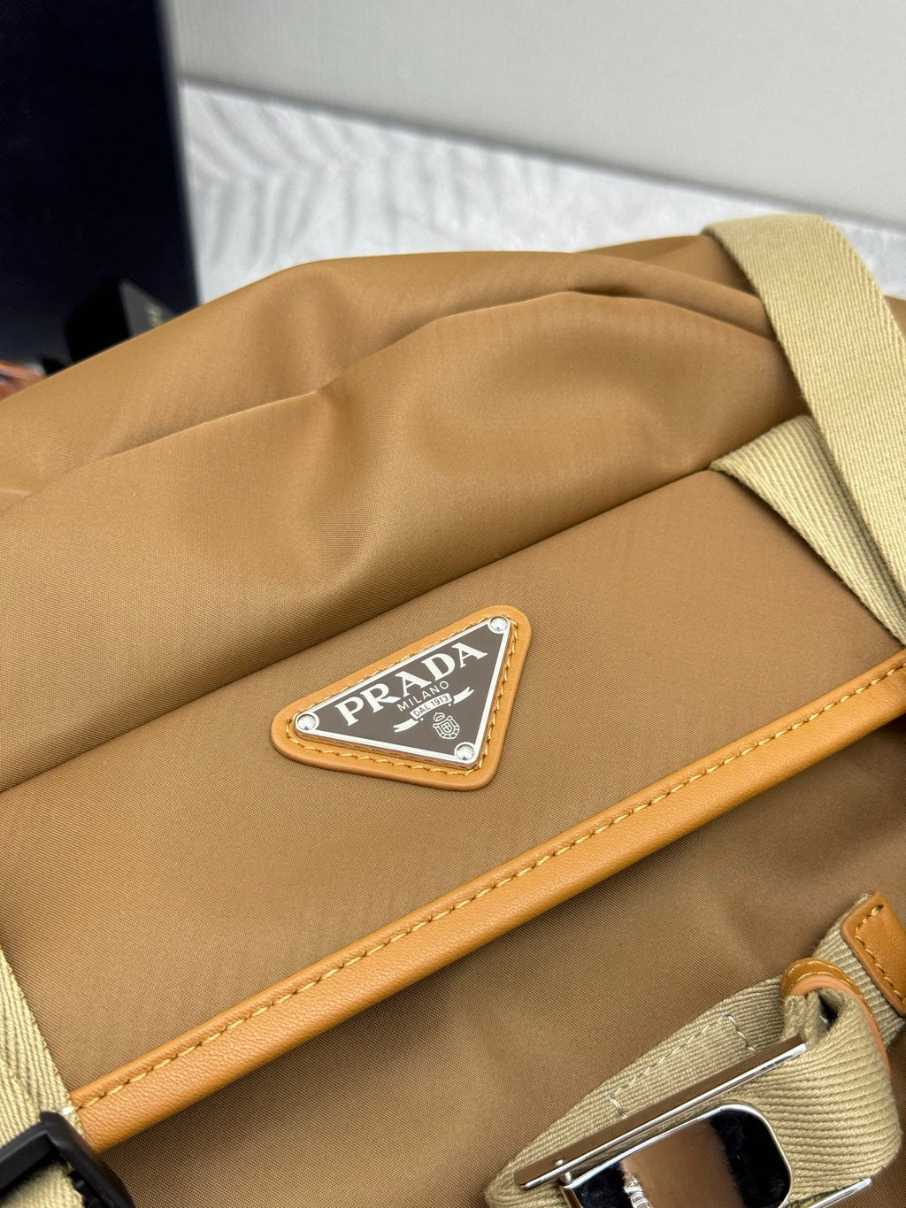 Prada tan backpack close-up of rectangular logo patch and leather trim along edge