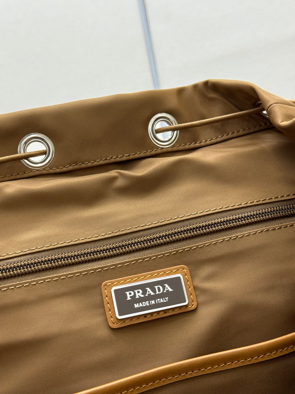 Prada tan backpack close-up of grommet detail, zipper, and logo label on flap