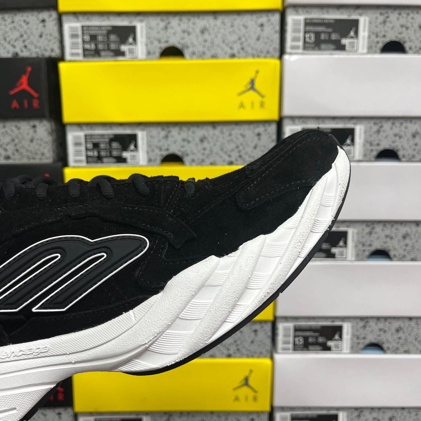 Black suede sneaker side view with white midsole and lace-up panel