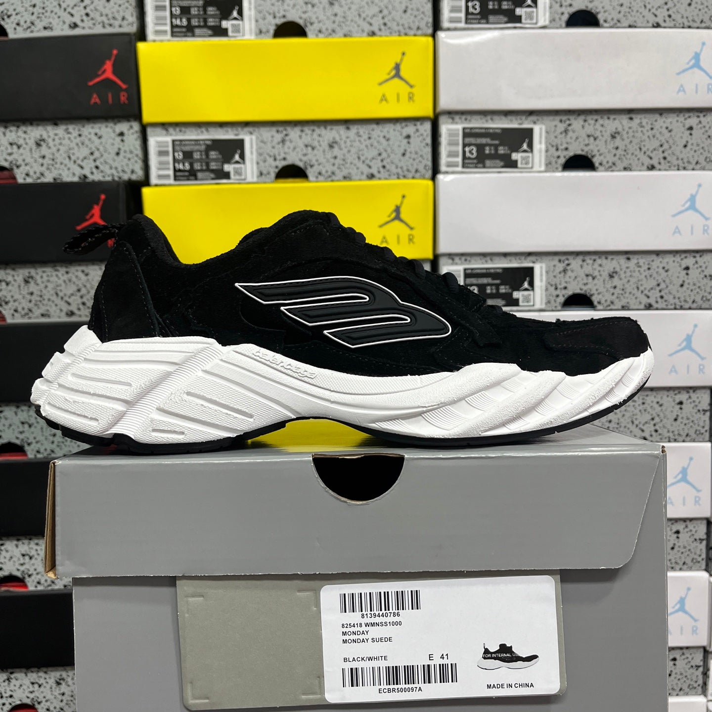 Black suede lace-up sneaker with white sole and side logo, angled view