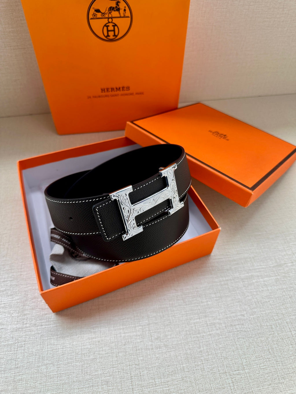 Black leather Hermes belt with silver buckle, resting in an open gift box.