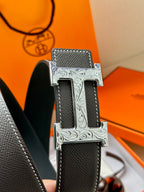 Close-up of black leather belt with silver engraved buckle featuring an H detail.