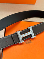 Black leather belt with silver engraved buckle, showing belt end with punched holes.