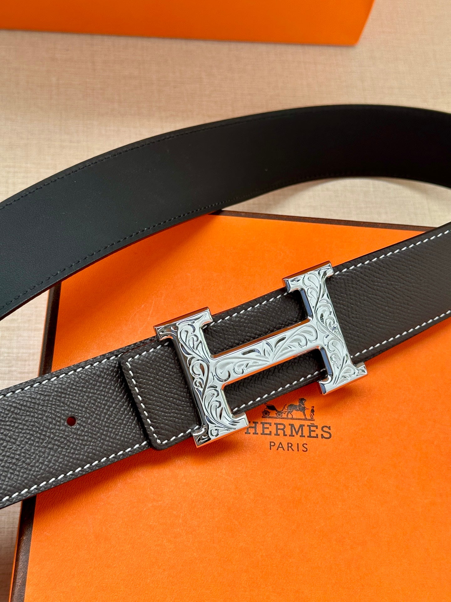 Black leather belt with silver engraved buckle, showing belt end with punched holes.
