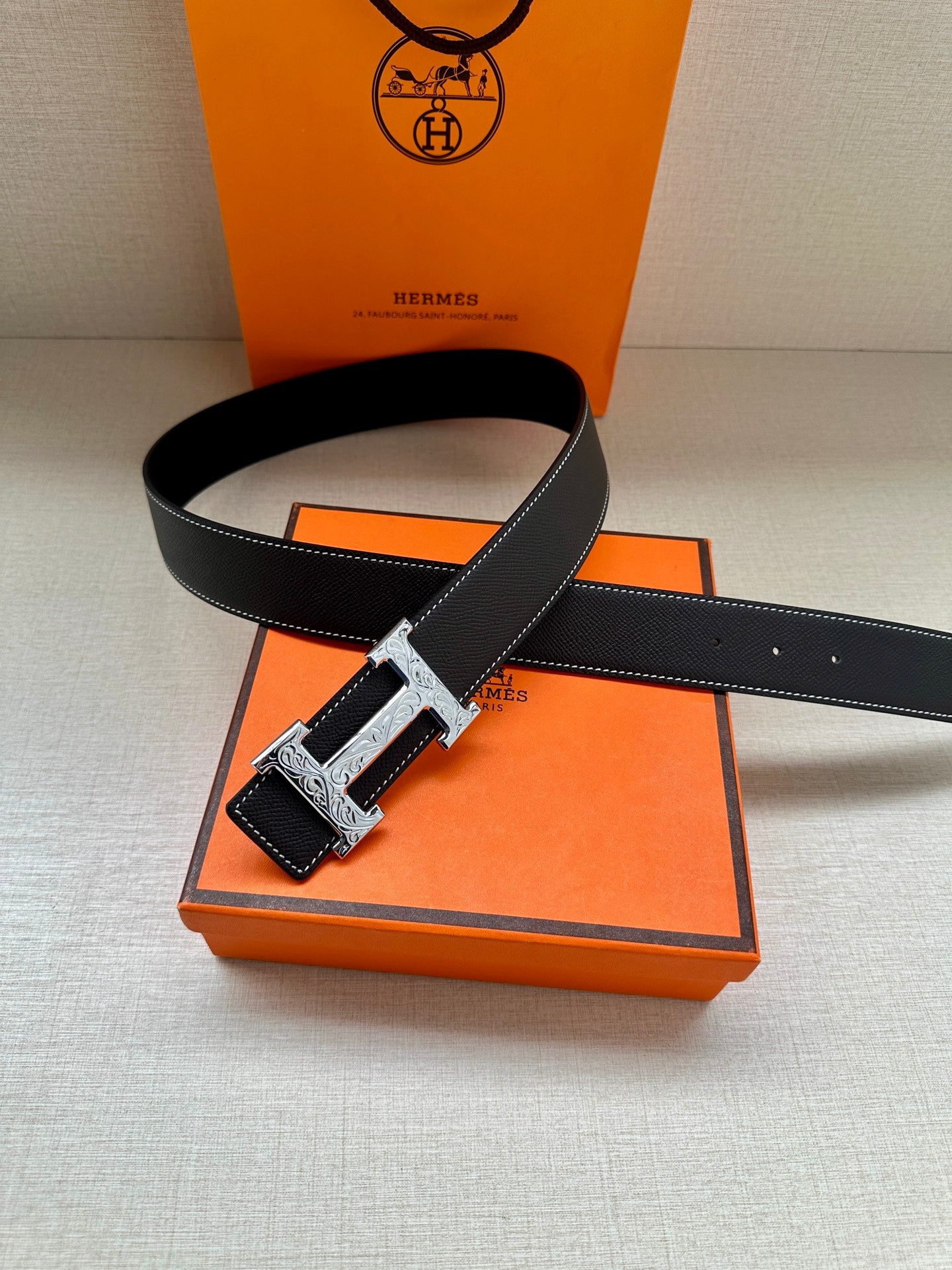 Black leather belt with silver H buckle and decorative keeper strap.