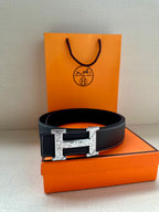 Black leather belt with silver square buckle and stitched edges on box.