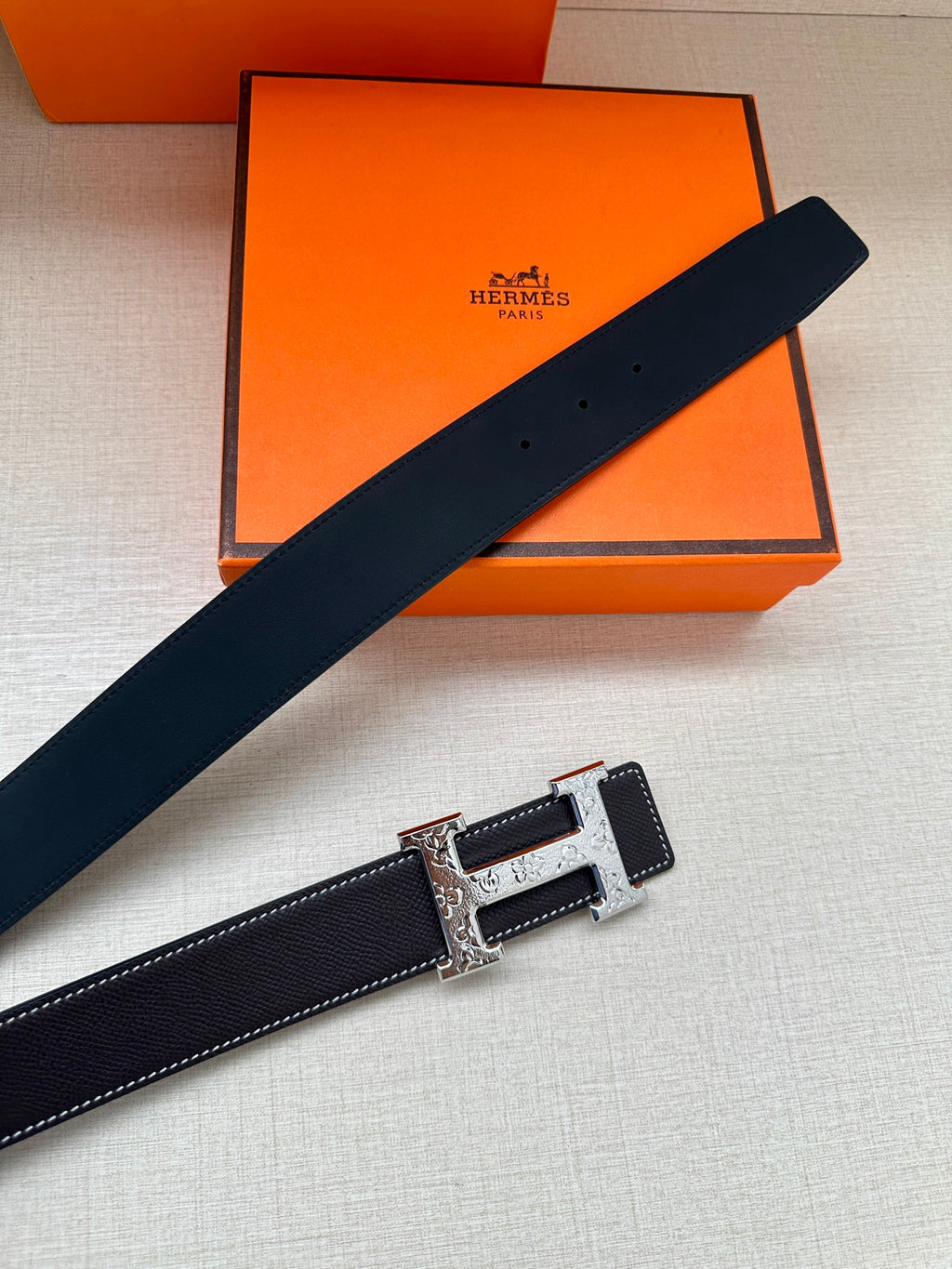 Dark navy leather belt laid diagonally with silver-tone buckle and engraved plate.