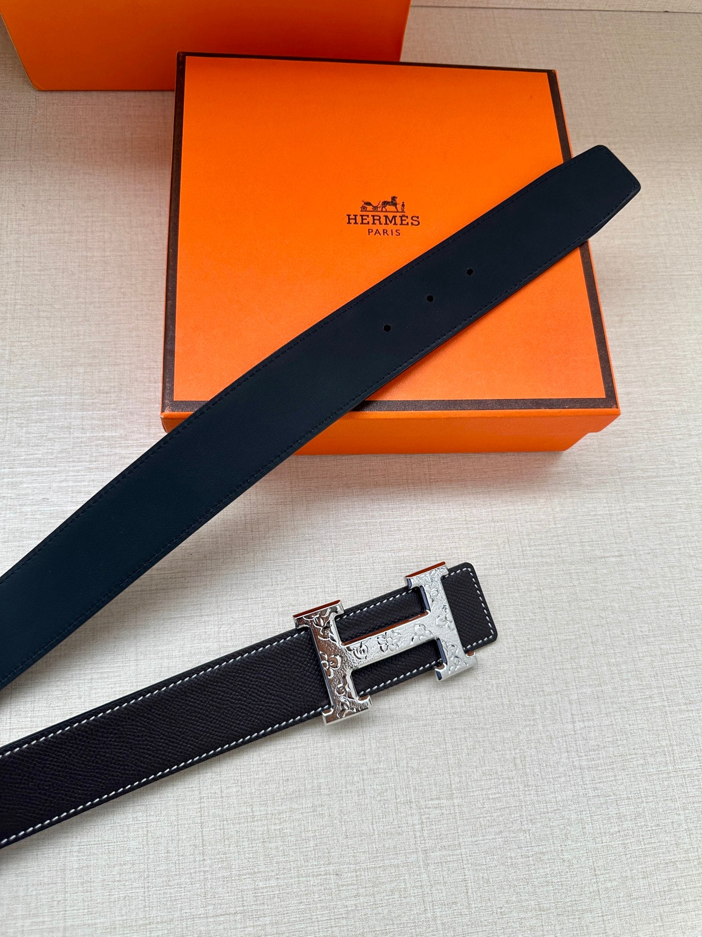 Dark navy leather belt laid diagonally with silver-tone buckle and engraved plate.