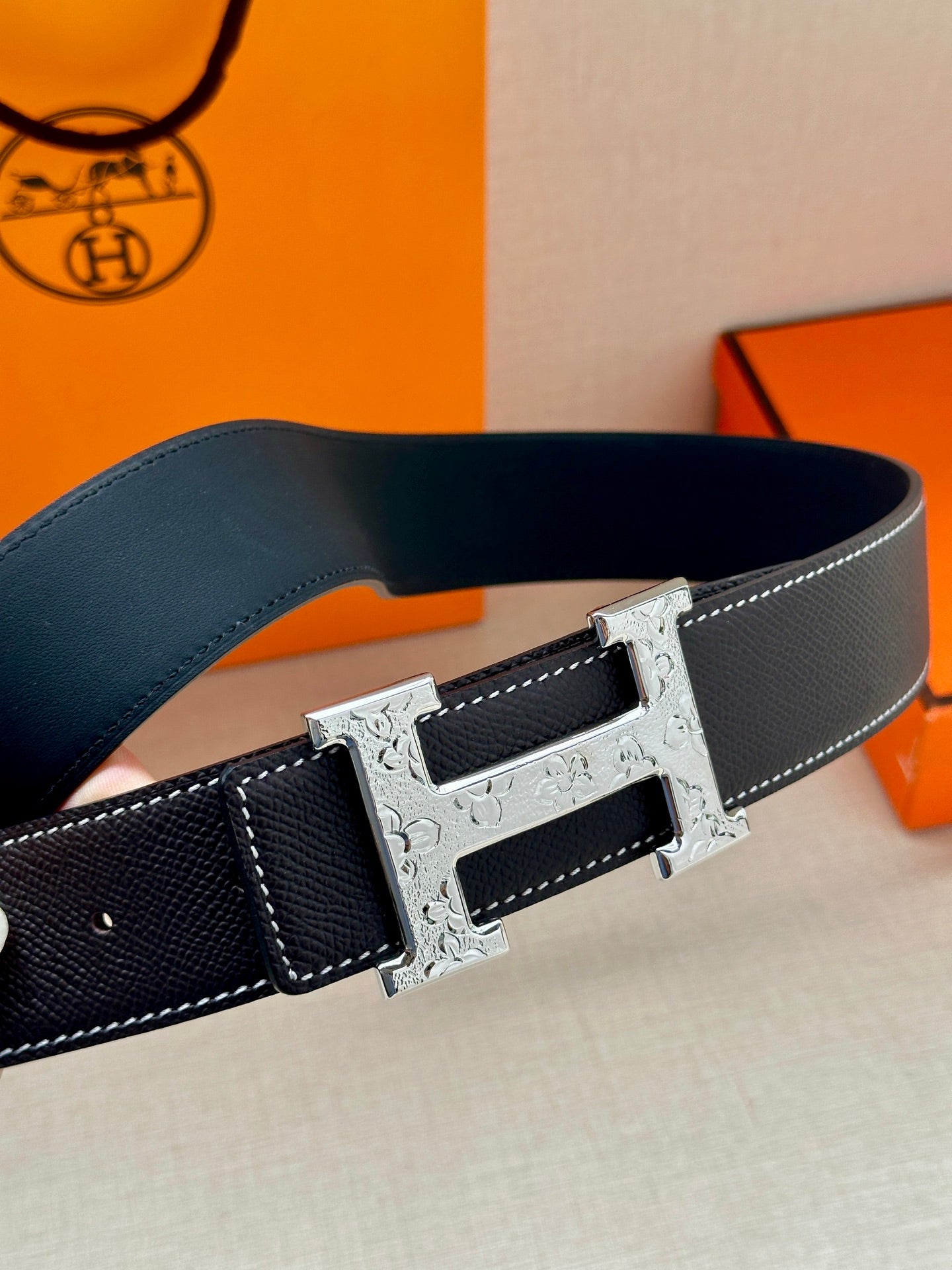 Dark navy leather belt close-up of silver-tone buckle with patterned metal plate.