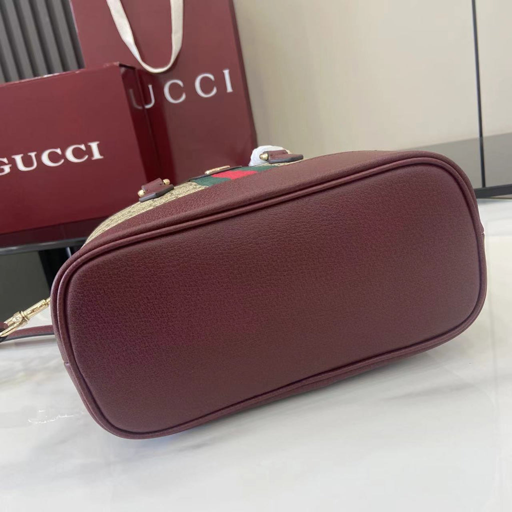 Gucci mini bag with burgundy textured leather, curved top, gold-tone clasp on front.