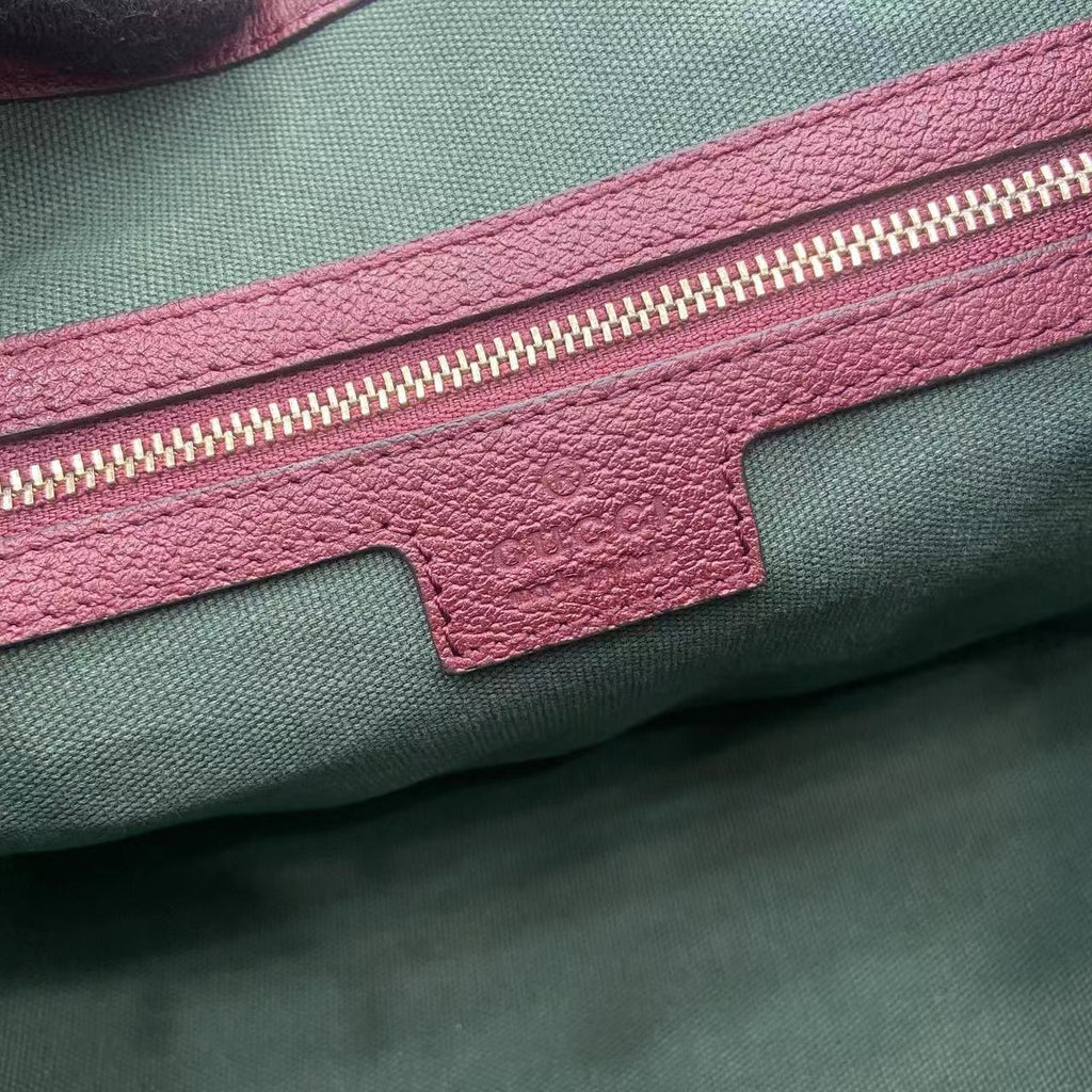 Gucci bag zipper pocket detail with burgundy leather edge and gold zipper on green lining.