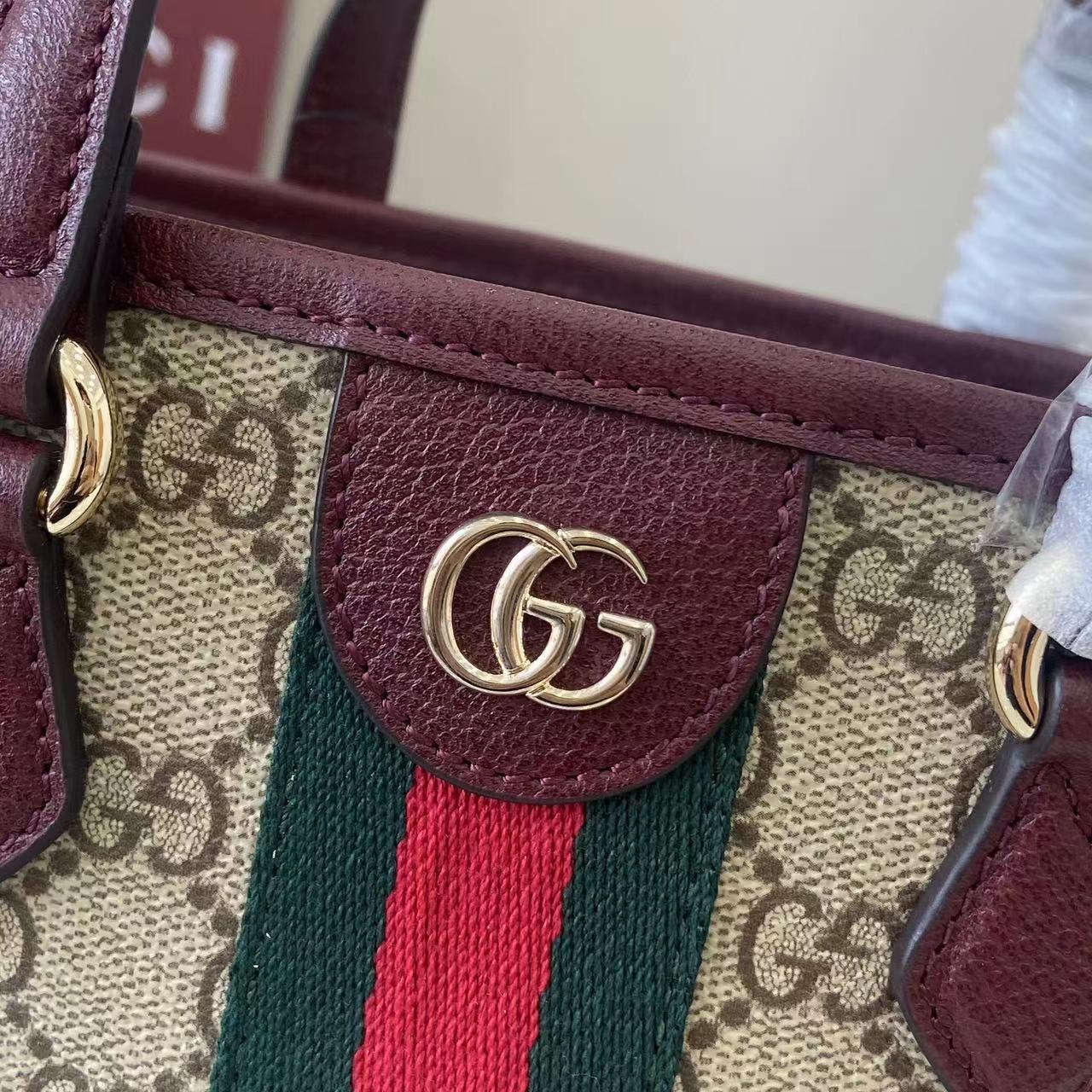 Gucci bag detail: burgundy leather tab with GG logo, GG canvas and green/red stripe.