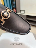 Close-up dark leather loafer toe with gold-tone emblem buckle detail