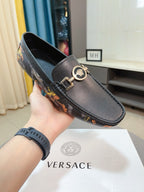 Dark luxury loafer held in hand, featuring gold-tone emblem buckle