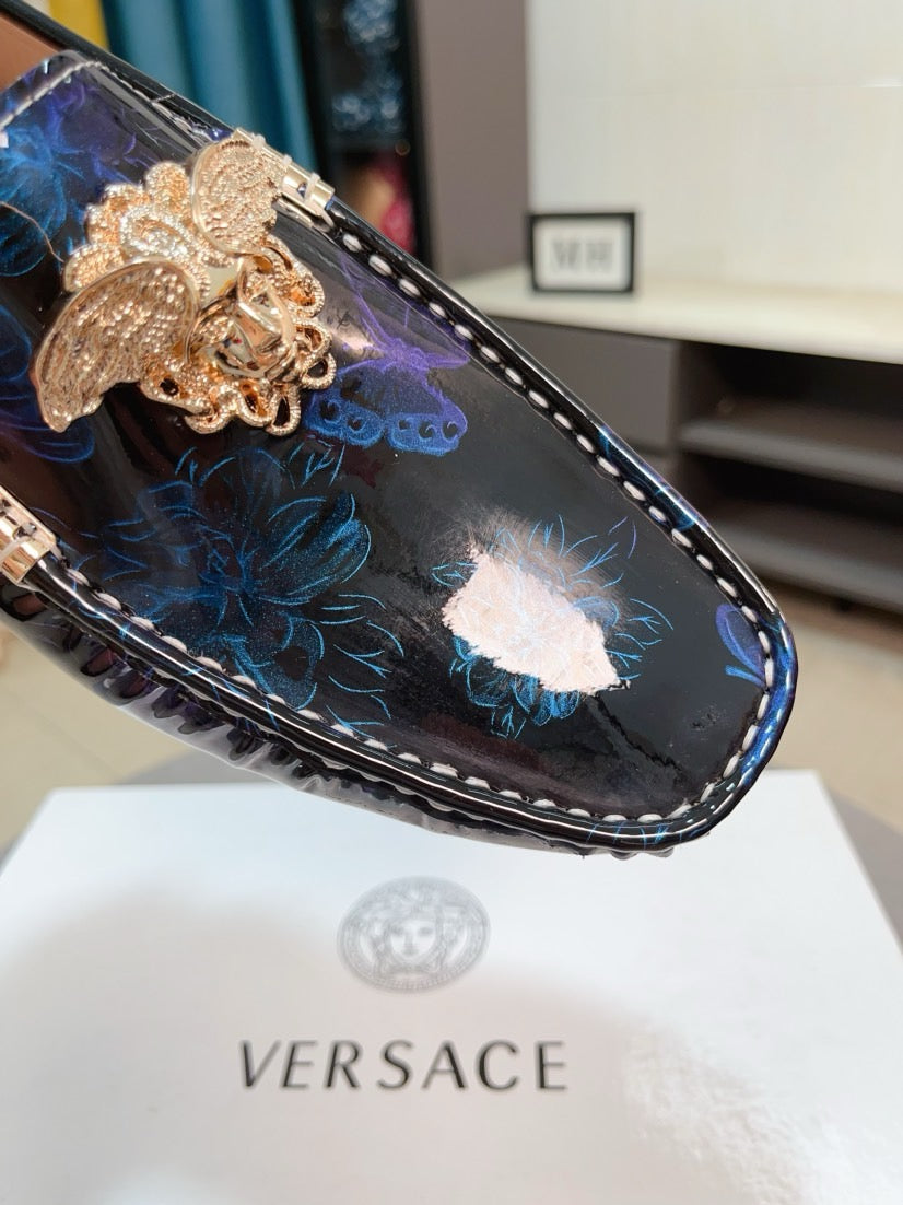 Close-up dark blue loafer with gold lion clasp over blue floral embroidery