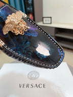 Close-up dark blue loafer with gold lion clasp over blue floral embroidery