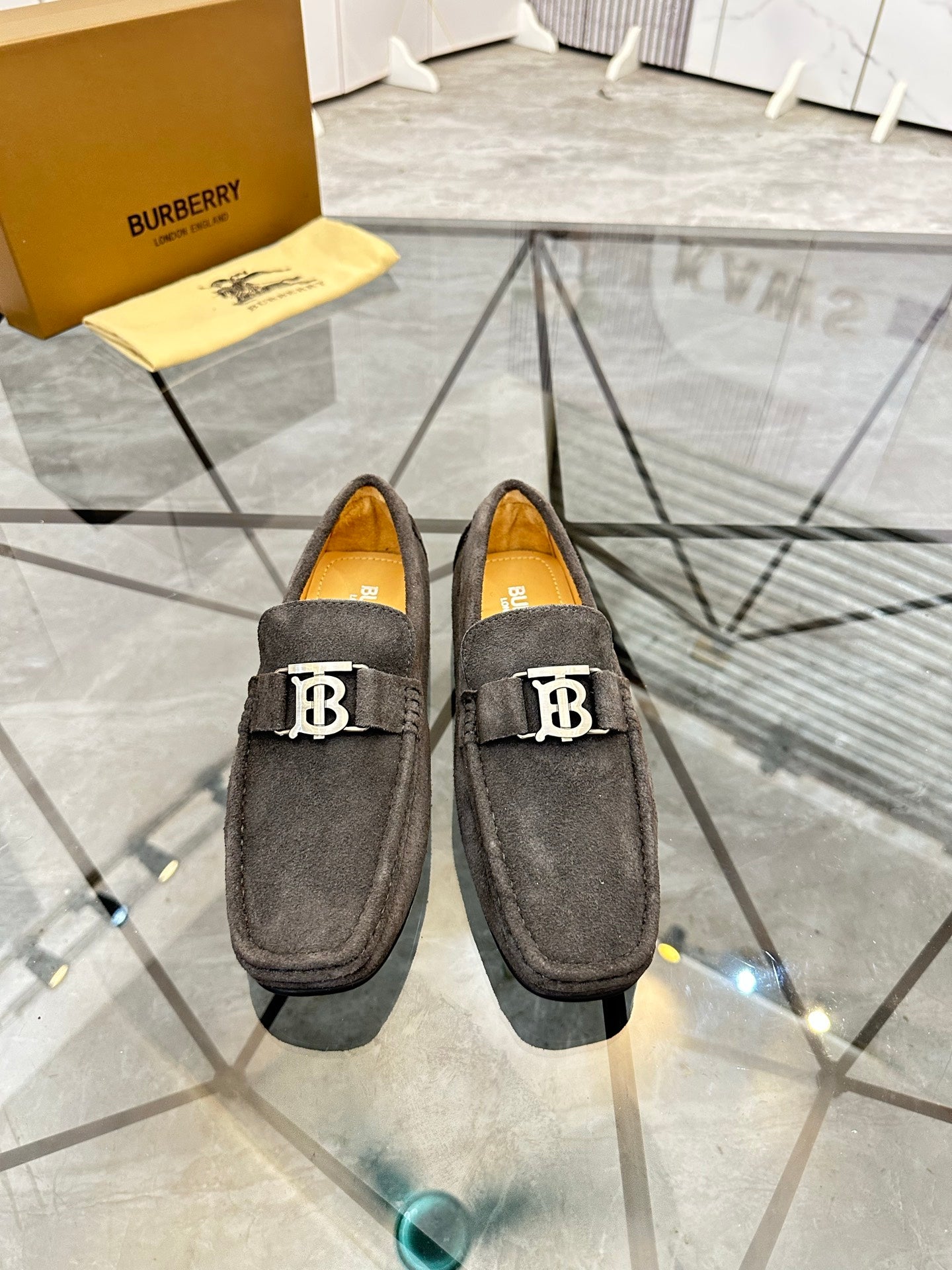 Black suede loafers with embossed B logo strap and tan interior lining