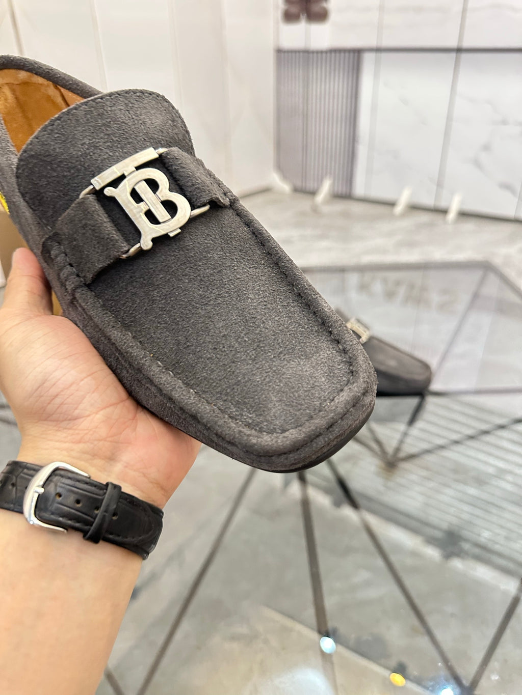 Close-up of dark gray suede loafer with gold-tone B buckle on strap
