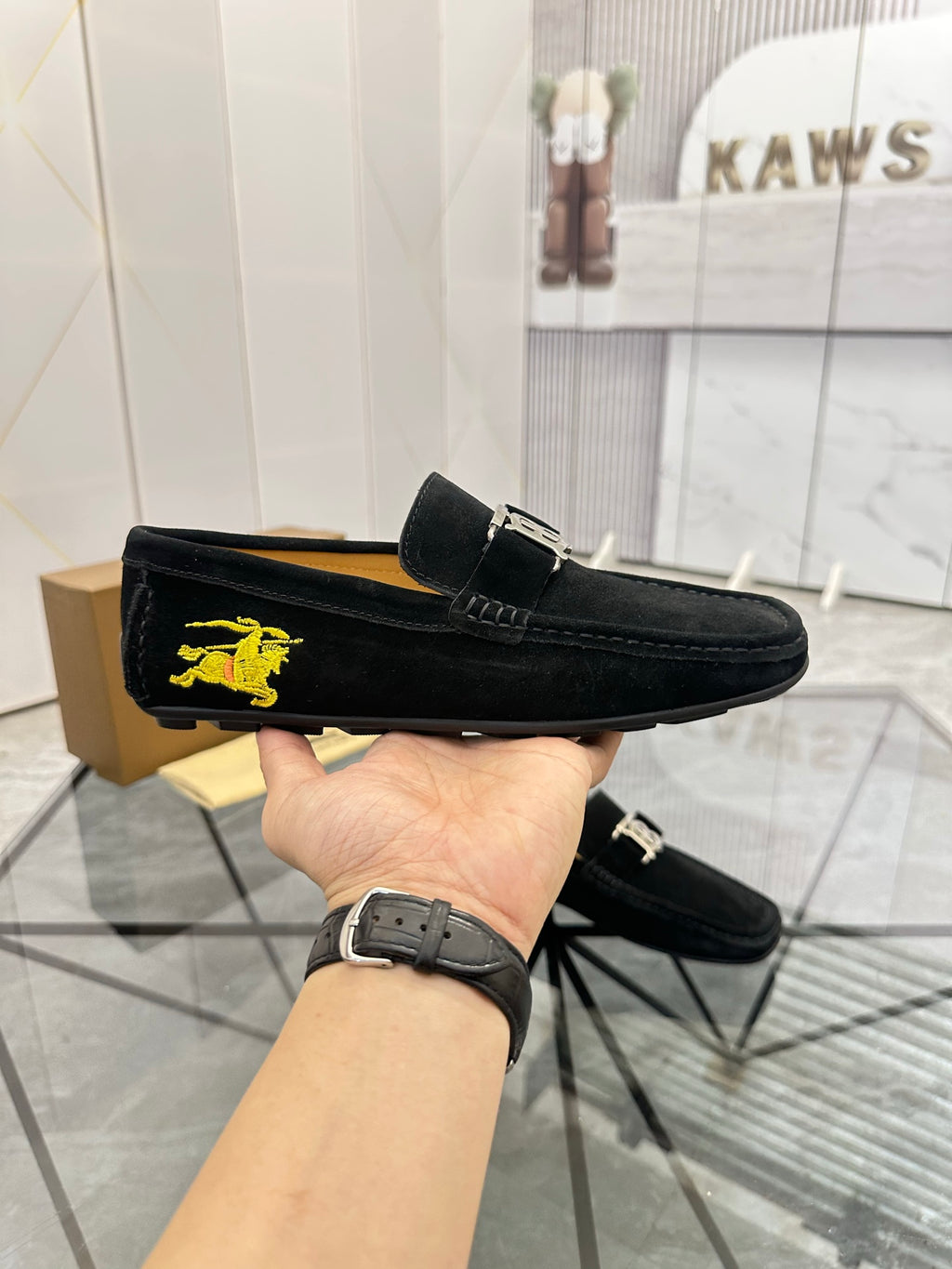 Burberry black loafer held up, with yellow horse emblem on the outer side