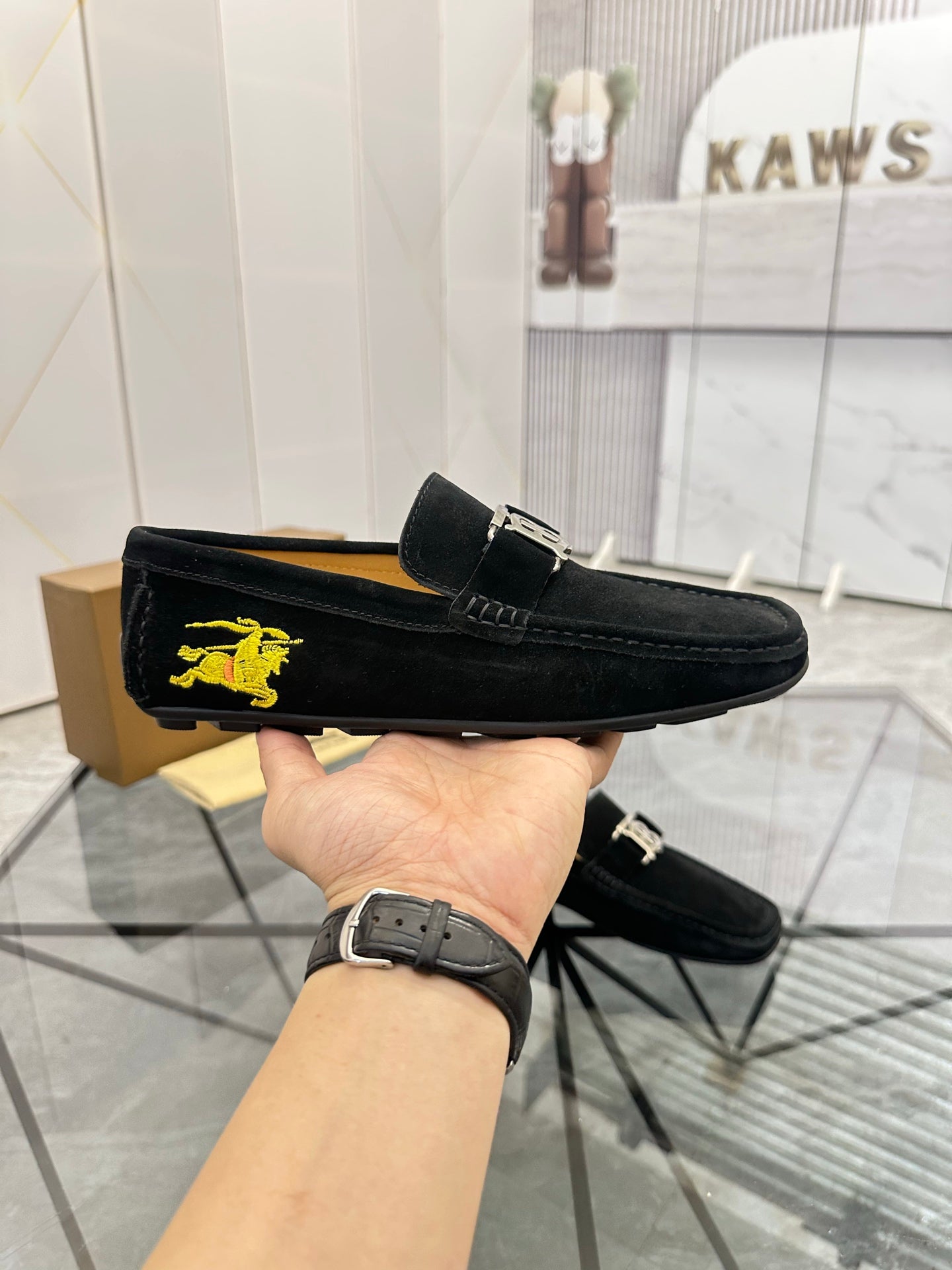 Burberry black loafer held up, with yellow horse emblem on the outer side