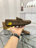 Brown suede loafer held up, featuring yellow horse emblem on the side and stitched sole.