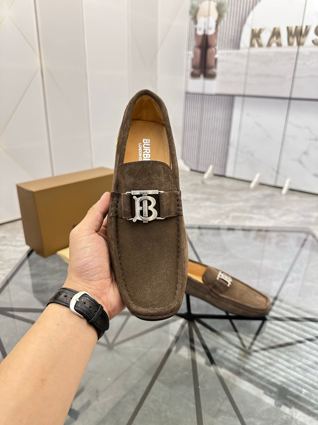 Brown suede loafer close-up with B logo strap detail and Burberry text on insole.