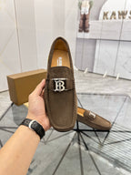 Brown suede loafer close-up with B logo strap detail and Burberry text on insole.