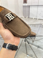 Brown suede loafer close-up with white B buckle and stitched moccasin-style edge.