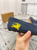 Navy suede loafer with yellow horse emblem on side, held near sole